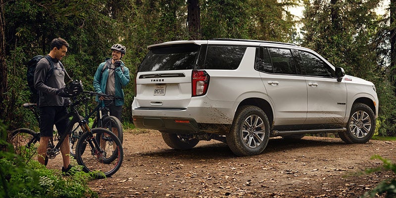 A white 2021 Chevrolet Tahoe parked on a dirt parking lot with two bikes talking behind it 