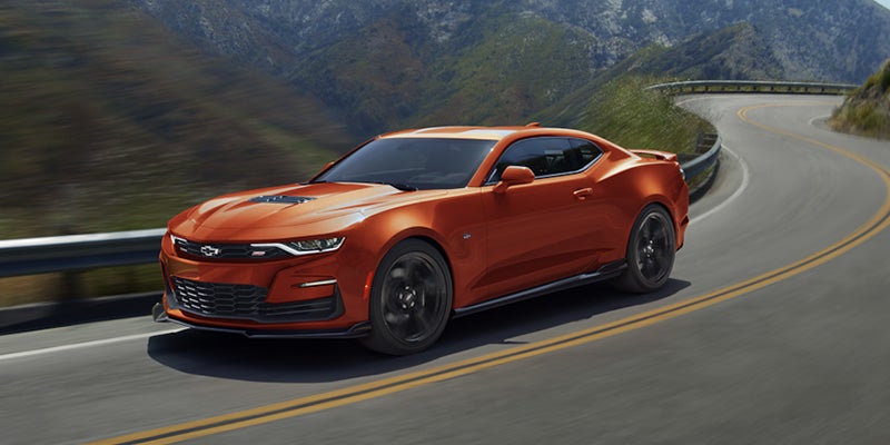 A orange 2024 Chevrolet Camaro, front-side view, driving on a winding road