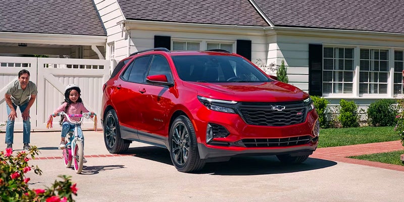 A red 2024 Chevrolet Equinox parked on a driveway with a girl on her bike and the dad behind her next to it 