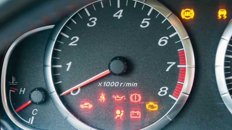 Car instrument cluster with the tachometer needle at zero and multiple warning lights lit, including check engine, ABS, oil pressure, battery, airbag, and seatbelt indicators.